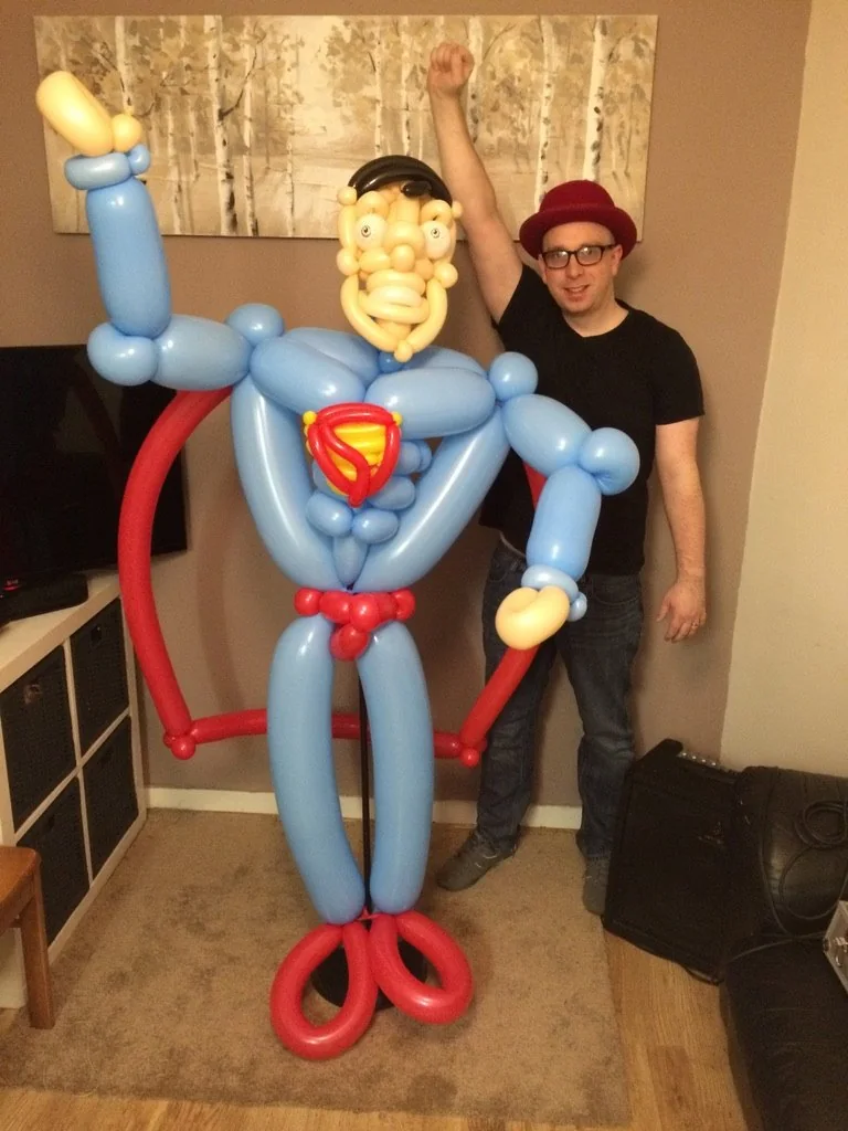 Benny standing beside a giant blue superhero-style balloon creation