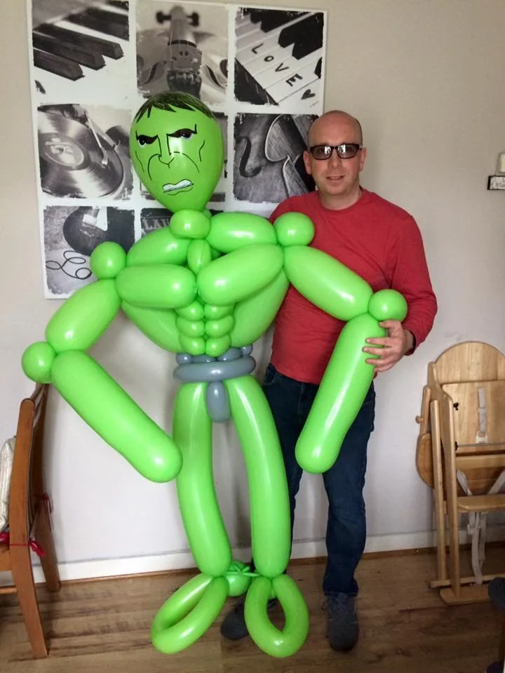 Benny standing beside a giant green superhero-style balloon creation